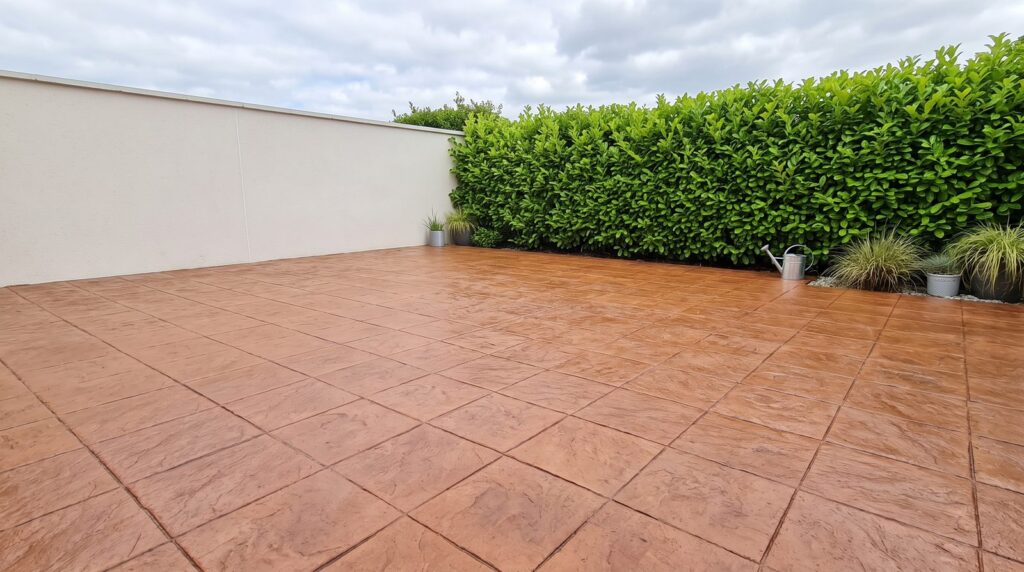 Terracotta pattern imprinted concrete patio bordered by a green hedge